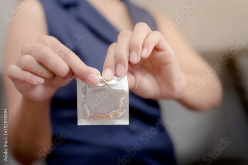 Woman hand holding condom sitting on sofa background,protection, safe sex,contraceptive means.