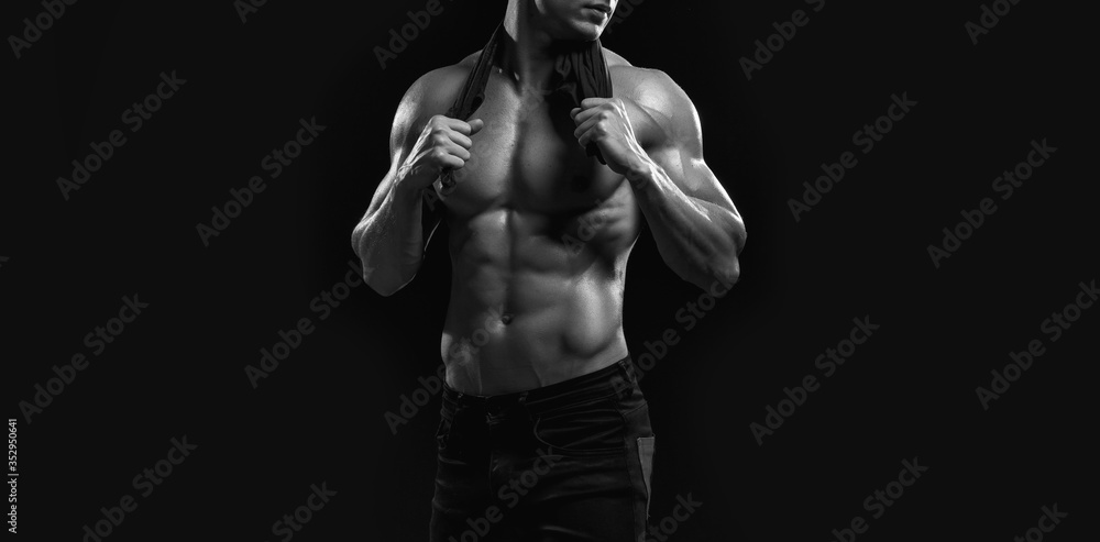Obraz premium Muscular model sports young man on dark background. Black and white fashion portrait of strong brutal guy. Sexy torso. Male flexing his muscles. Sport workout bodybuilding concept.