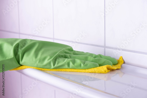 cleaning lady in green gloves in the bathroom washes a shelf in green gloves