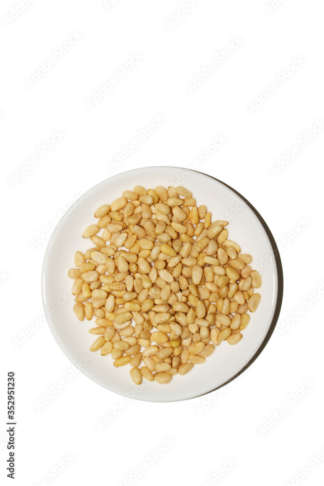 Organic food. Pine nuts on a white background. Cedar nuts flatlay on a white saucer. Agricultural concept. Superfood, top view, copy space. Banner vertical format with empty space for your text Organic food. Pine nuts on a white background. Cedar nuts flatlay on a white saucer. Agricultural concept. Superfood, top view, copy space. Banner vertical format with empty space for your text