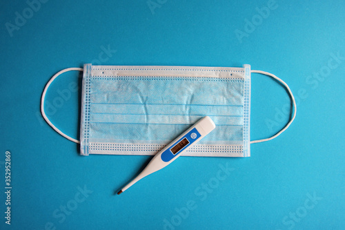 High fever (40 degree) displayed on clinical thermometer lying on op mask and turquoise background view from above photo