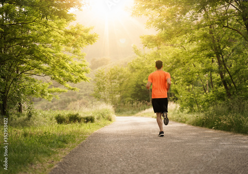 boy with orange shirt during a run in the woods. Flare and light effect, scenic shot. Low point of view. Ideal for concept of fredoom, happiness and adventure.