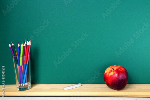 Green school board with colored pencils and an apple.