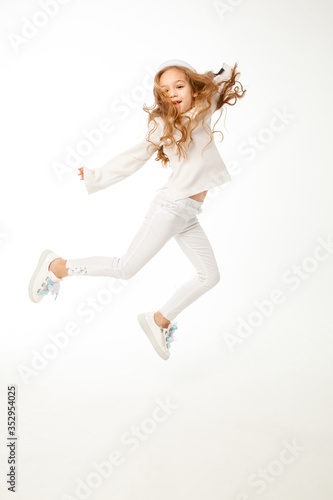 A girl with long hair, dressed in white colored clothes, is jumping on a white background.
