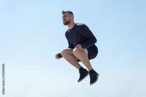 Portrait of a young bearded athlete of twenty-five, jumping against a blue sky.