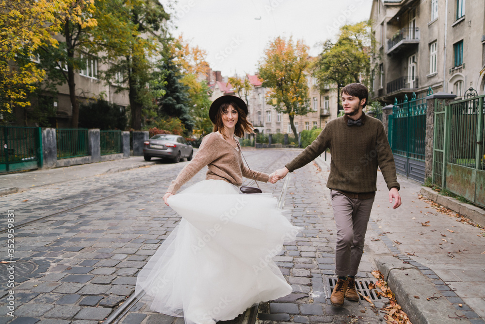 Naklejka premium Romantic and happy caucasian couple in casual wedding clothes walking and hugging at the city streets. Love, relationships, romance, happiness, urban concept. Man and woman celebrate their marriage.