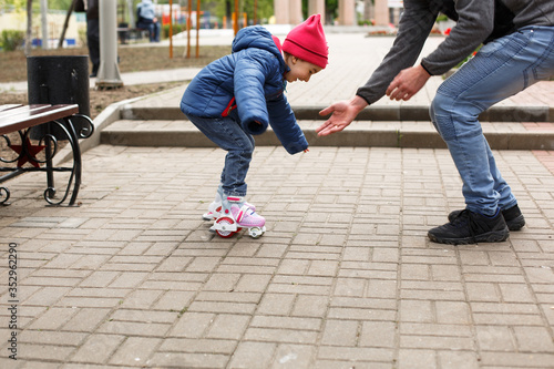 Dad teaches his little daughter to ride four-wheeled roller skates. The father supports the child by the hands, feet of the father and the child in skates. Focus on the rollers. Father's day, family 