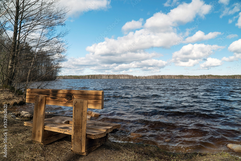 Wooden bench on the lake with white clouds in the sky.