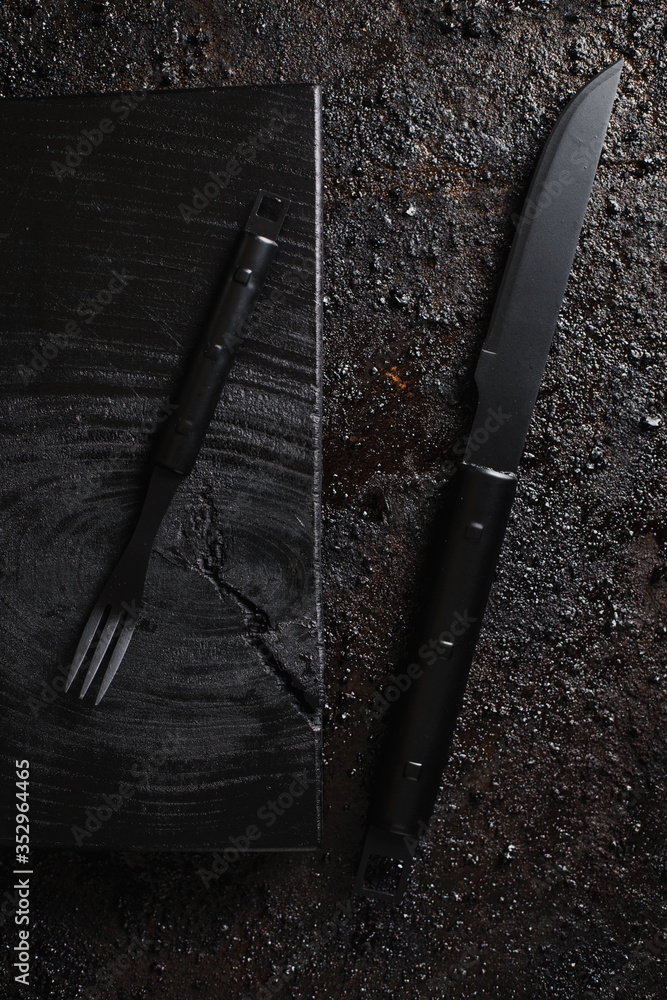 Knife and for on pice of black wood and black texturated background.
