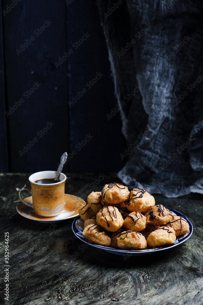 Delicious profiteroles on black textured background and a cup of tasty coffee.