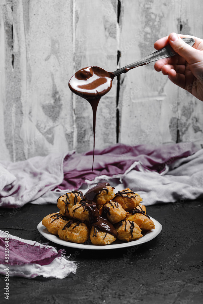 Delicious profiteroles on black textured background with a creative decoration, and liquid chocolate on top
of them.