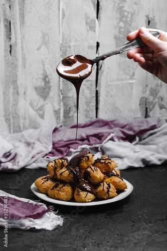 Delicious profiteroles on black textured background with a creative decoration,  and liquid chocolate on top
of them.