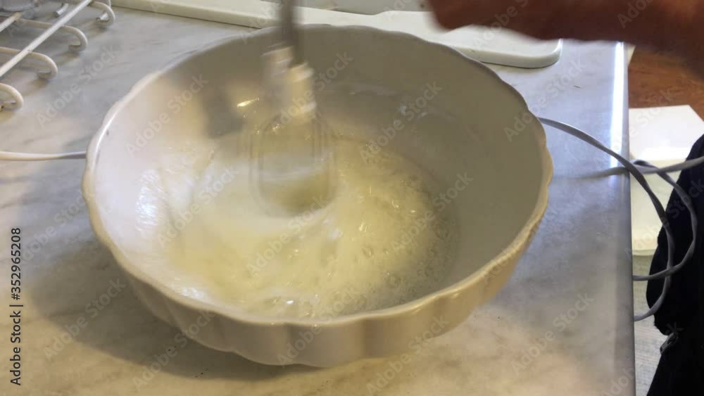 A mother with an accessory whips the egg whites until stiff, as an ingredient for the cake for her family. A mother with an accessory whips the egg whites until stiff, as an ingredient for the cake for her family.