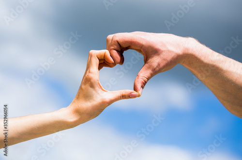 Female and man hands in the form of heart against the sky. Hands in shape of love heart. Heart from hands on a sky background. Girl fnd male hand in heart form love blue sky. Love, friendship concep