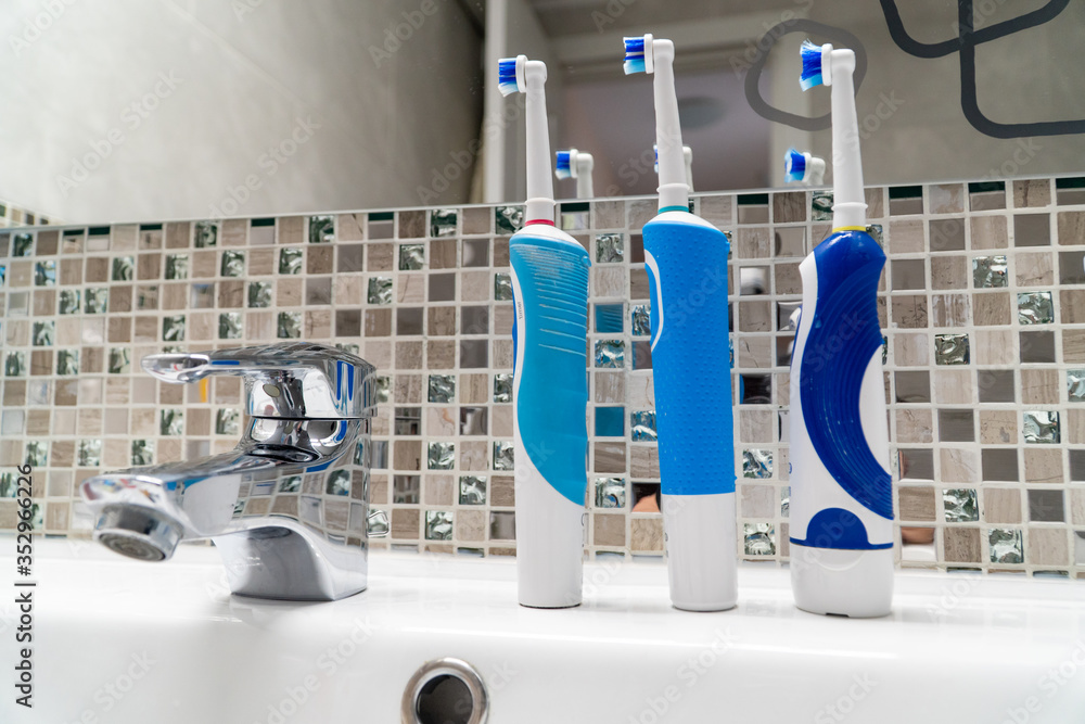 Three electric toothbrushes stand on the washbasin.