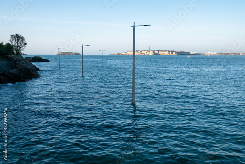 Dinard, France 24-05-2020. Ocean tide view of the flooded port road in the distance the cities of Saint Malo and Intramuros. Street lanterns protruding into the water
