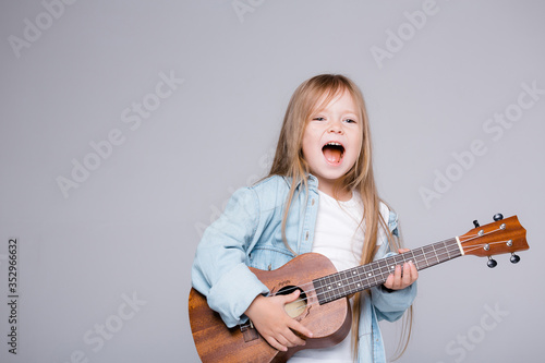 The girl sings and plays the ukulele. The child laughs, poses for the camera and enjoys the music. Learning to play ukuleles
