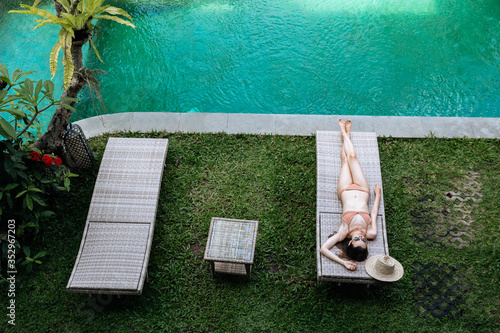 Top view of slim woman in beige bikini take sunbath on lounge chair at the poolside near luxury pool in tropic on vacation.