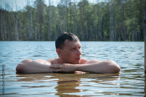 Man is swimming in a pond on green forest background.