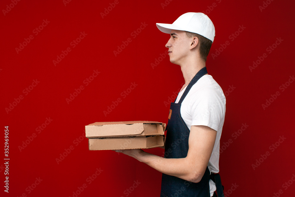 pizza delivery man in uniform on a red background gives boxes of food, the courier guy gives the finished order pizza delivery man in uniform on a red background gives boxes of food, the courier guy gives the finished order