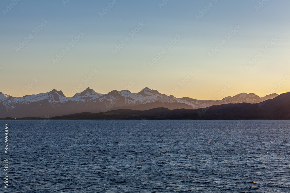 A mystical fjord in Norway with mountains and fog hanging over the water in polar day. midnight sun, selective focus