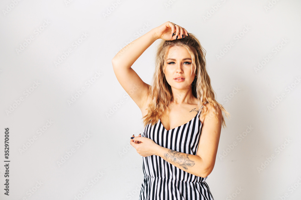 Tattooed girl posing in studio. Attractive young woman in striped dress looking at camera with a passion Tattooed girl posing in studio. Attractive young woman in striped dress looking at camera with a passion