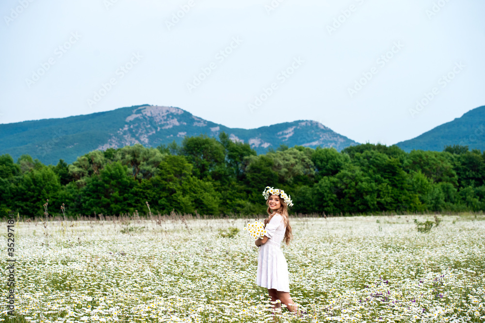 Beautiful young girl with curly hair in chamomile field.  Beautiful girl with chamomile wreath on flowering field in summer. Beautiful curly hair. Freedom concept.