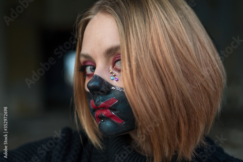 beauty portrait of a beautiful girl in a black mask with rhinestones, cool designer makeup. The girl is crying emotionally, holding a broken glass in her hand.