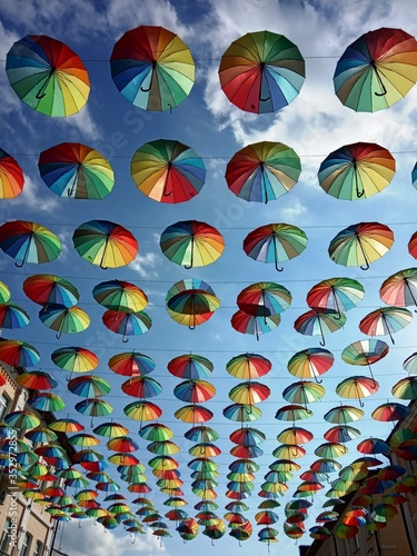 Multi-colored umbrellas in rows hang over the pedestrian street of the city on a May warm sunny day.