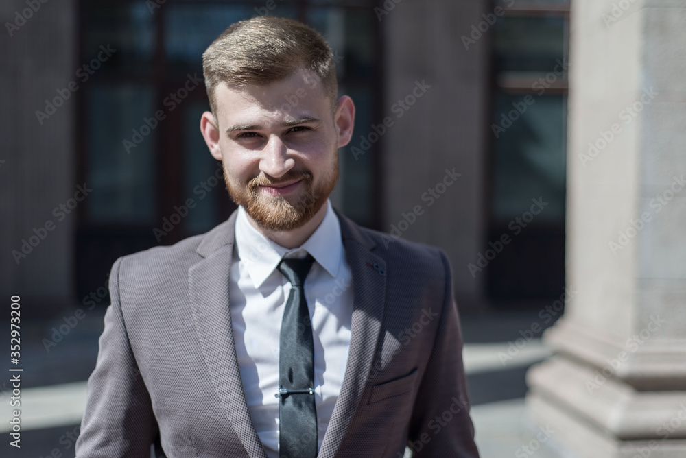 Portrait of a young bearded guy of twenty-five years old, in a business suit, against the background of an office building. Posing looking at the camera. Outdoors Portrait of a young bearded guy of twenty-five years old, in a business suit, against the background of an office building. Posing looking at the camera. Outdoors