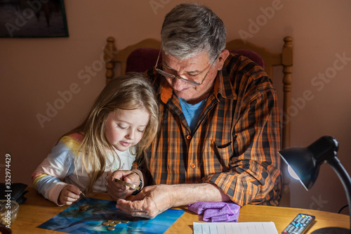 Grandfather shows coins to a small beautiful granddaughter through a magnifier. The concept of common interests and family unity. Family values.