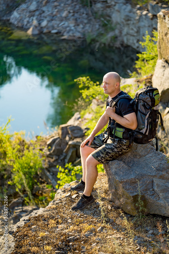 A traveler sits on a stone with a backpack on his shoulder. Rocks background. A man enjoys nature around him.