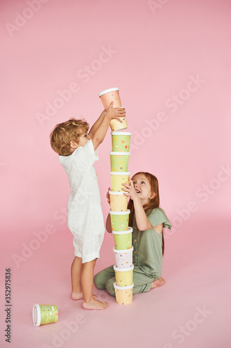 Children build a tower of colored paper boxes on a pink background.