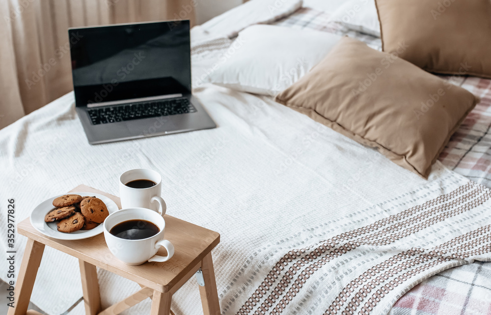 Breakfast in bed with laptop. Hot coffee with oatmeal cookies with chocolate on a wooden tray. Breakfast in bed with laptop. Hot coffee with oatmeal cookies with chocolate on a wooden tray.
