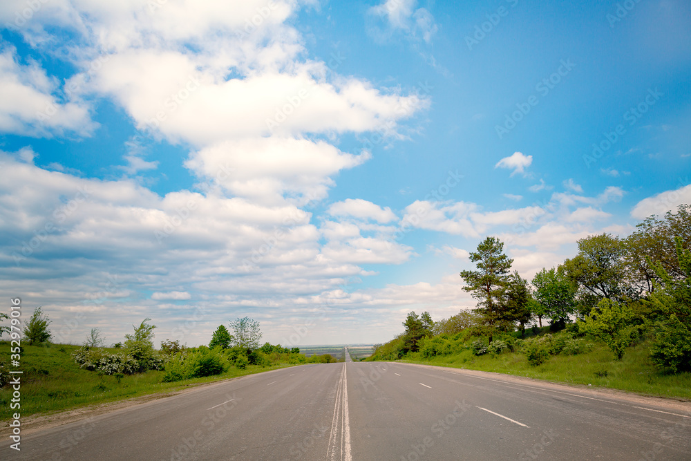 Open road through the green field and clouds on blue sky in summer day