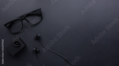 Black fashion men accessories, glasses, earphone, camera on black texture background with copy space for text, Flat lay, business desk from top view