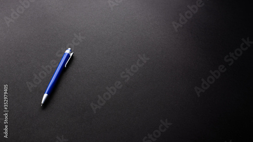 Blue plastic pen on black texture background, office desk table from top view, copy space. 