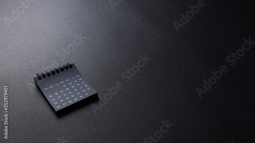 Black calendar on black texture background, office desk table from top view, copy space. 