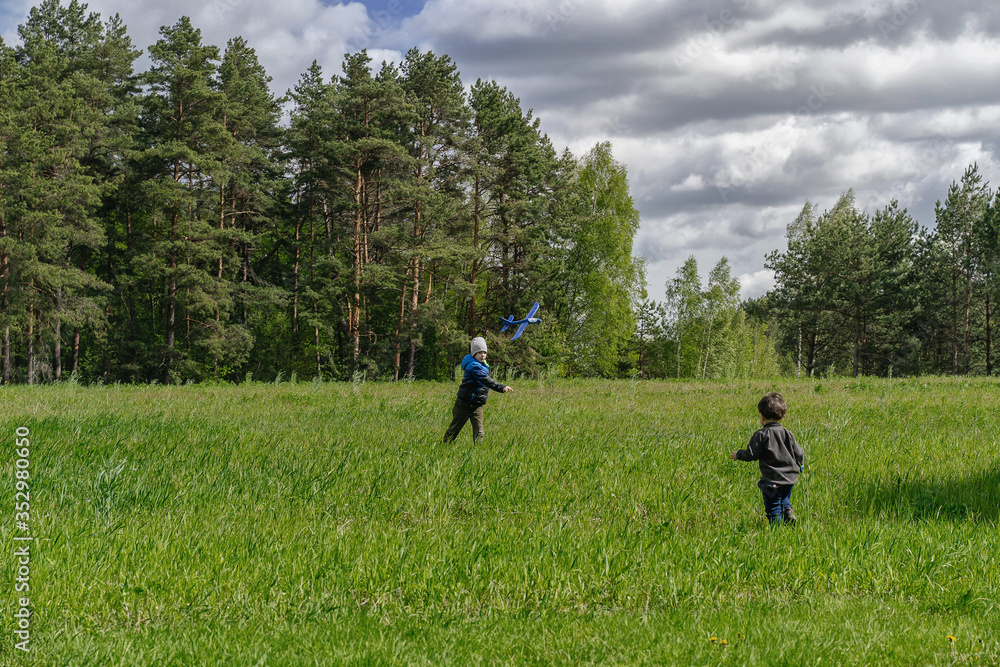 Children play airplane in a green field. Blue model of the plane in flight. 