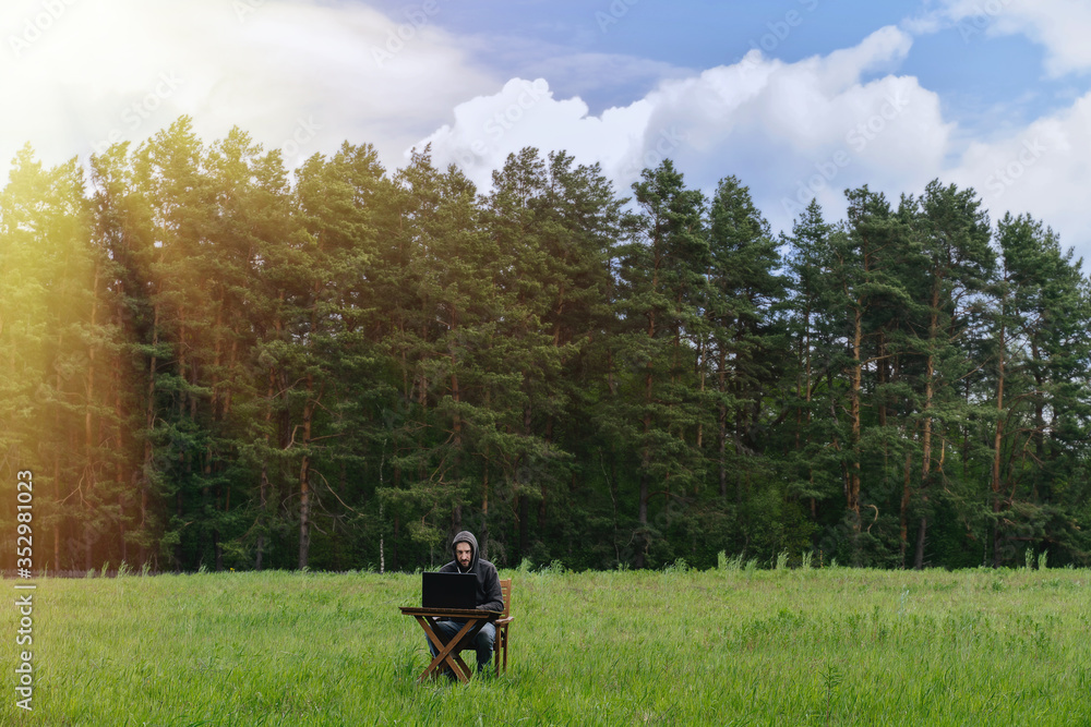 Fototapeta premium A man works at a table with a laptop in an empty field. Remote work in the field