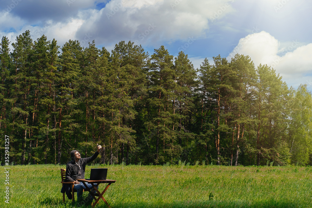 Obraz premium A man works at a table with a laptop in an empty field. Remote work in the field