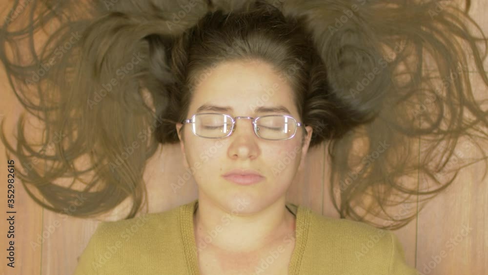Top view Shot Close-up portrait of joyful young woman with beautiful hair and glasses Laying on Floor Concept of Happiness Milennial Cheerful Lifestyle Hipster and Tenderness She lays on the ground Top view Shot Close-up portrait of joyful young woman with beautiful hair and glasses Laying on Floor Concept of Happiness Milennial Cheerful Lifestyle Hipster and Tenderness She lays on the ground