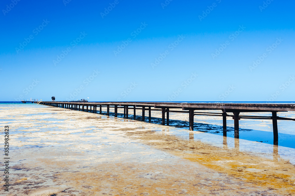 Beautiful view of the tropical coast with a long pantone. A large wooden pier is on the sandy beach of the resort. Landscape of the sea coast