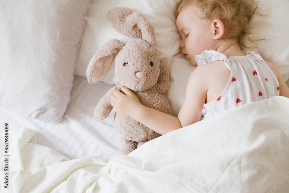 Cute child little girl sleeping in bed with white linen hugging her soft toy teddy bunny. Cute child little girl sleeping in bed with white linen hugging her soft toy teddy bunny.