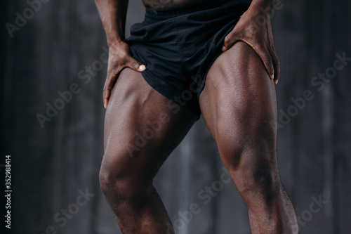 Close-up front muscles of the upper thigh of a black professional athlete in black shorts.