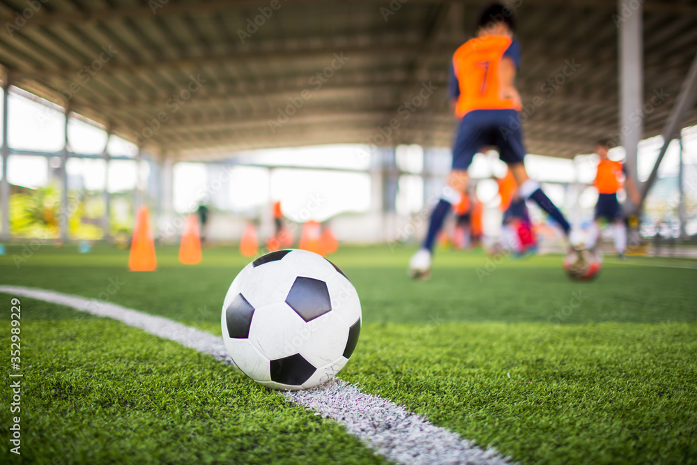 Football on green artificial turf with blurry soccer team training.