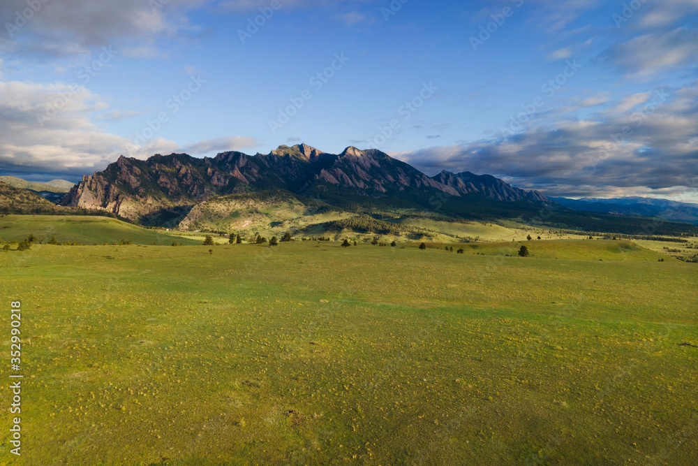 Fototapeta premium morning sun over green meadow and flatiron mountains with blue sky and clouds colorado