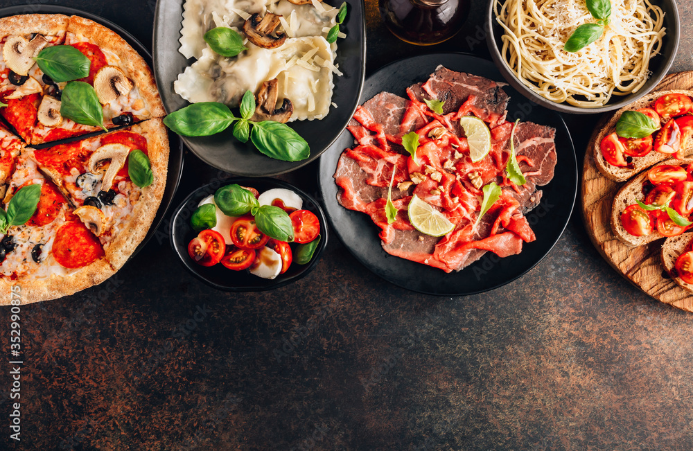 Full table of italian meals on plates Pizza, pasta, ravioli, carpaccio. caprese salad and tomato bruschetta on black background. Full table of italian meals on plates Pizza, pasta, ravioli, carpaccio. caprese salad and tomato bruschetta on black background.