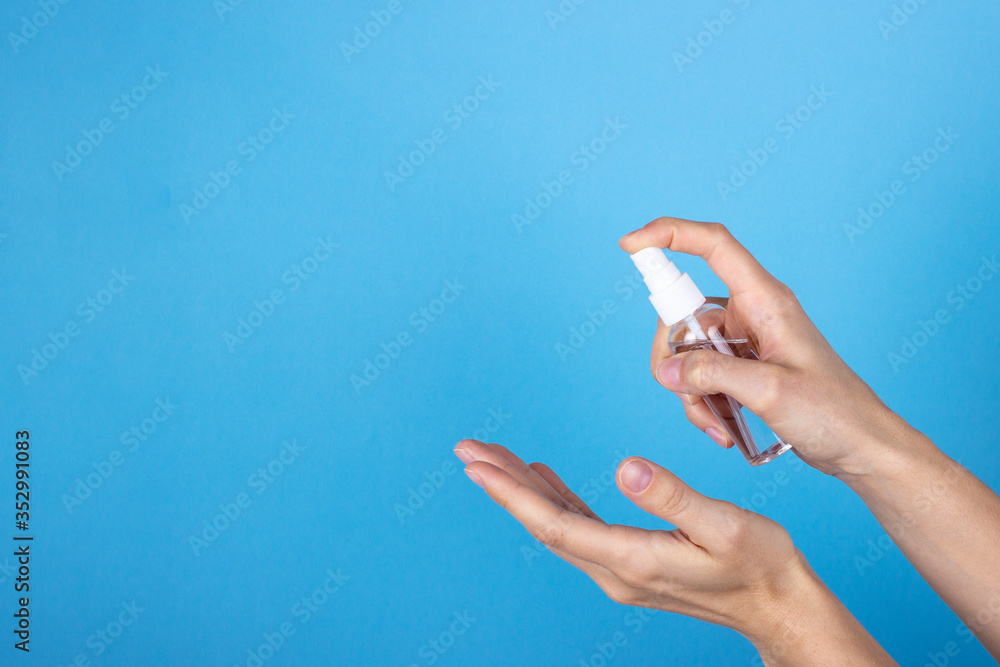 A young woman is holding an antiseptic on blue background.The disinfectant is sprayed on the hands.Lady's hands are treated with an antibacterial agent to maintain hygiene and protect against viruses. A young woman is holding an antiseptic on blue background.The disinfectant is sprayed on the hands.Lady's hands are treated with an antibacterial agent to maintain hygiene and protect against viruses.