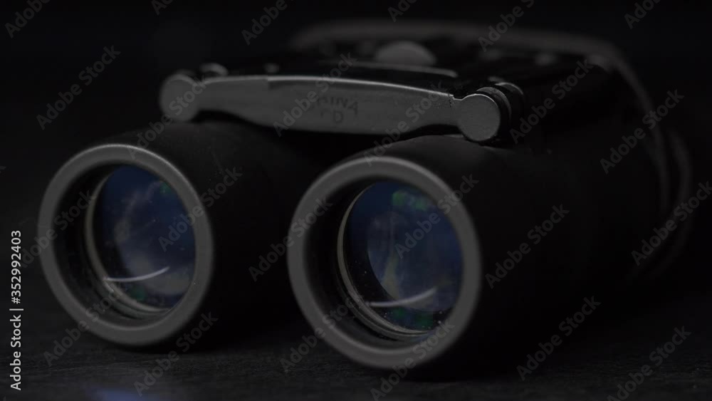 Dramatic Closeup of light illuminating a pair of binoculars on a table in the dark while it passes over it Dramatic Closeup of light illuminating a pair of binoculars on a table in the dark while it passes over it